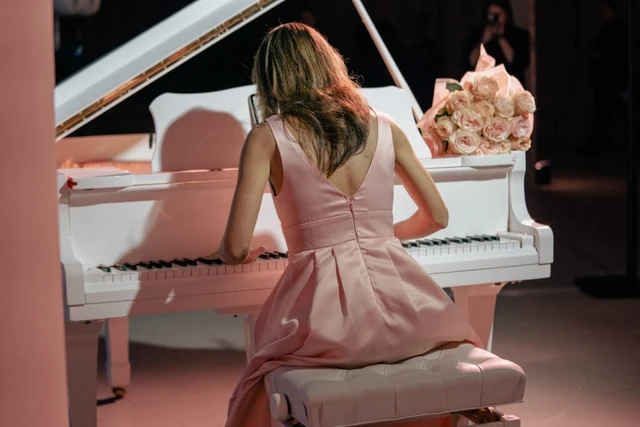Giulia Vazzoler seen from behind at a white grand piano, a bouquet of pink roses beside her