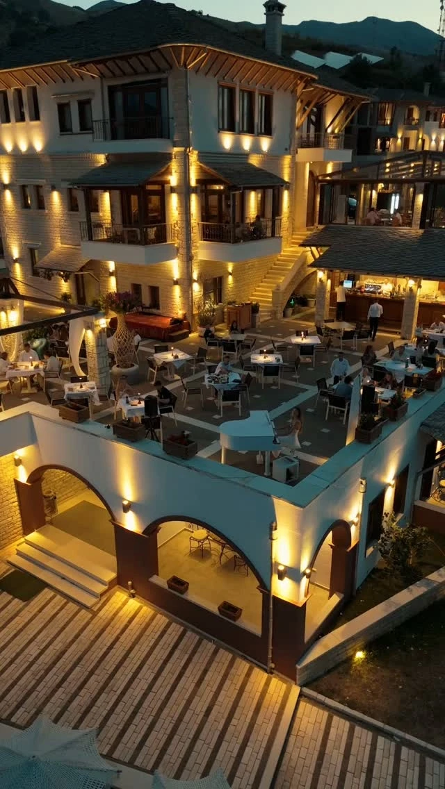 A white hotel with lit terraces at night, tables set below