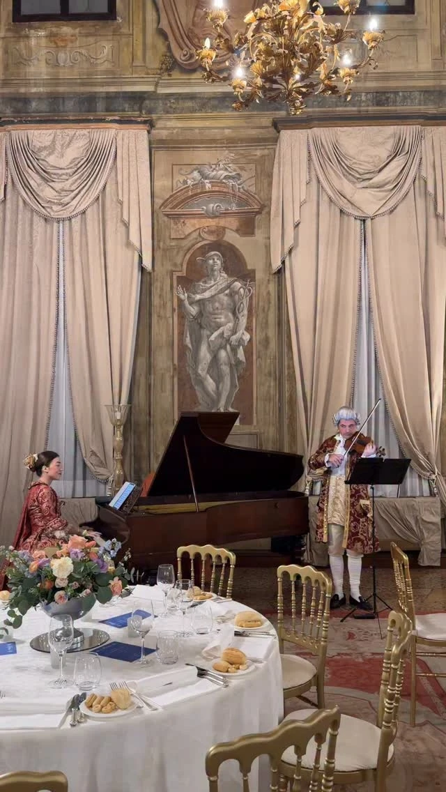 A grand piano in a frescoed hall, round tables laid for dinner